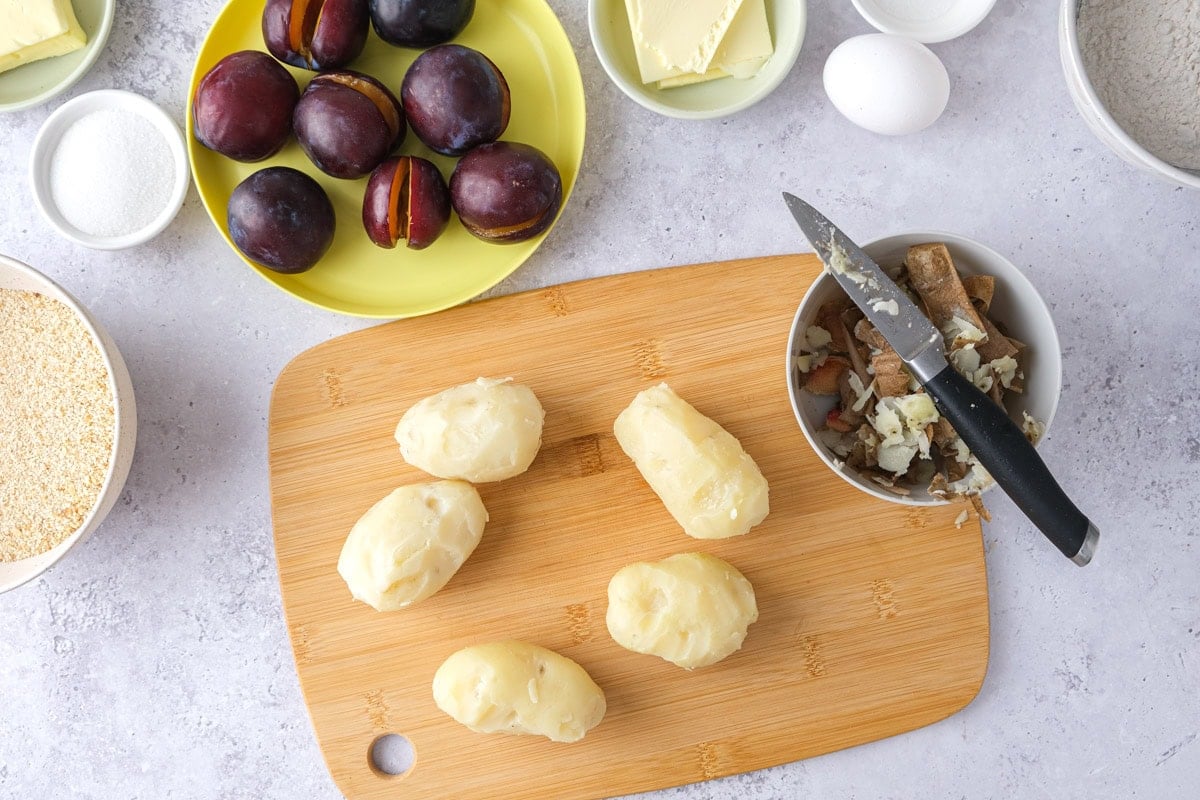 boiled and peeled potatoes on wooden cuting board with knife and skins beside.