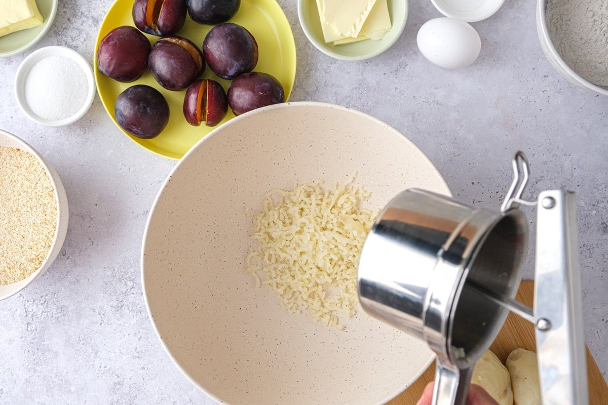 metal press squeezing potatoes through into mixing bowl on counter.