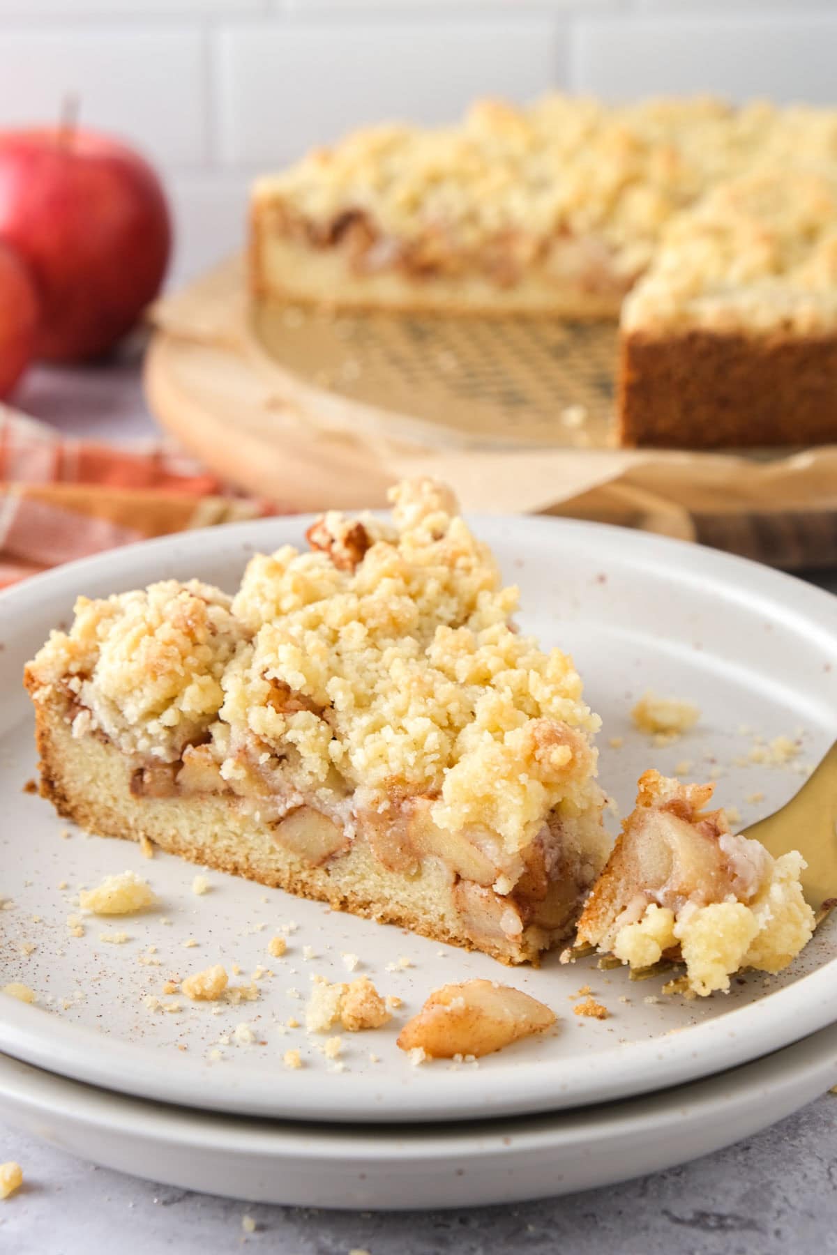 slice of german apple cake on plate with whole cake behind on counter.