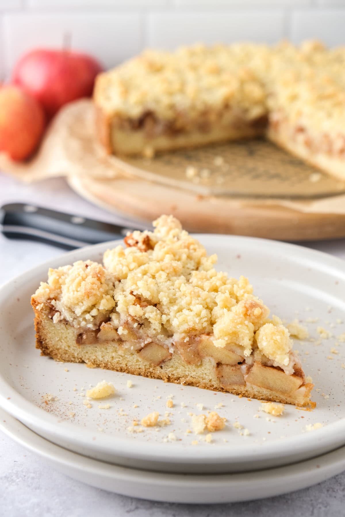 slice of german apple cake on plate with more cake behind.