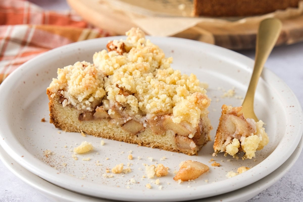 slice of german apple cake on plate with golden fork removing some.