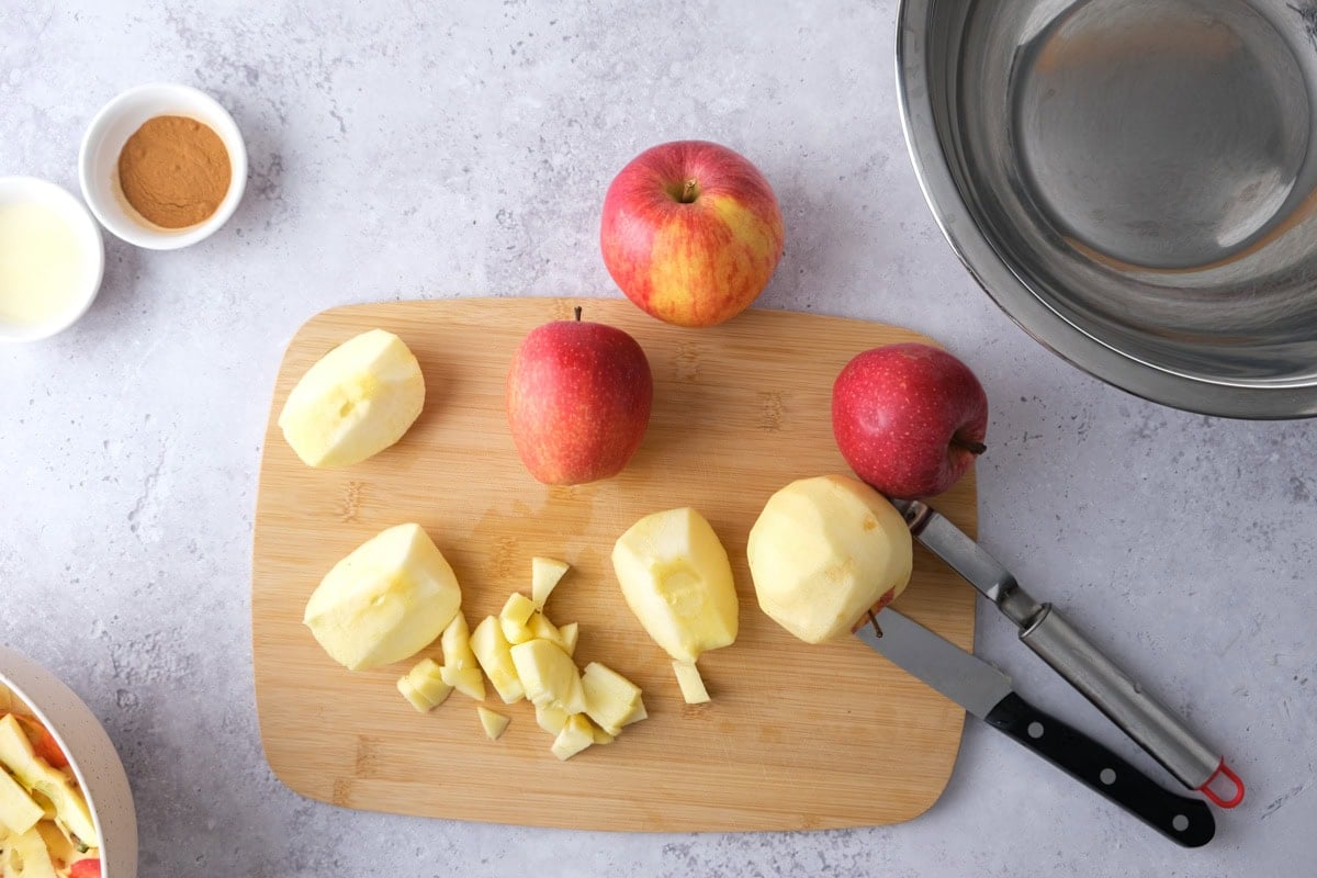 red apples being cut up into pieces on wooden cutting board.