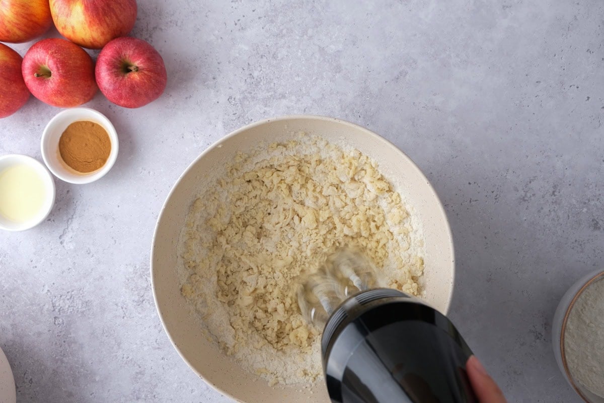 electric mixer blending dough ingredients in large bowl on counter.